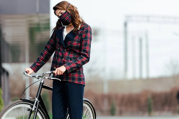 戴着格子呢面具的女商人在外面的自行车旁用智能手机交谈 — 图库照片