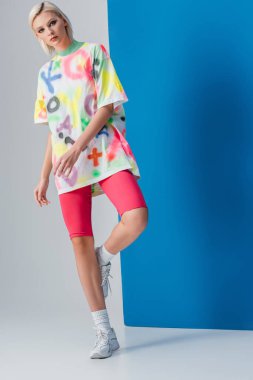 Neon pembe bisiklet şortu ve gri-mavi renkli tişörtle poz veren şık sarışın kız. 