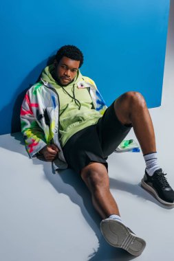 Yakışıklı, modaya uygun Afrikalı Amerikalı adam gri ve maviye renkli fütürist bir görünüm takınıyor.