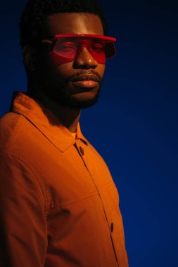 Fütürist görünümlü ve kırmızı ışıkta mavi poz veren şık Afro-Amerikan erkek modeli. 