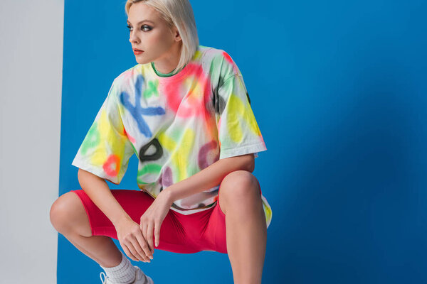 fashionable woman posing in neon pink bike shorts and colorful t-shirt on grey and blue 