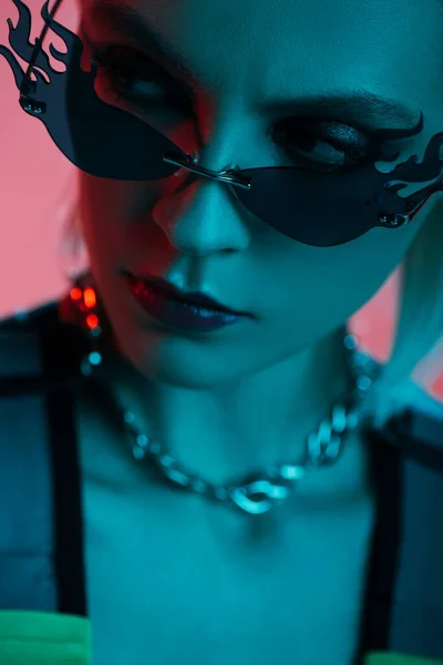 未来的なレオタードと炎の形をしたサングラスのスタイリッシュな女性モデルは ブルーライトでピンクに隔離されたポーズ — ストック写真