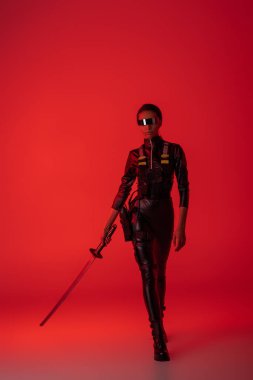 Kırmızı arka planda kılıcı olan, gözlüklü, Afro-Amerikalı bir kadın.