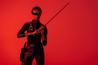 futuristic african american woman in glasses with sword isolated on red background clipart