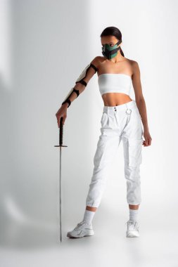 Beyaz arka planda kılıç taşıyan, güvenlik maskeli fütürist Afrikalı Amerikalı kadın.