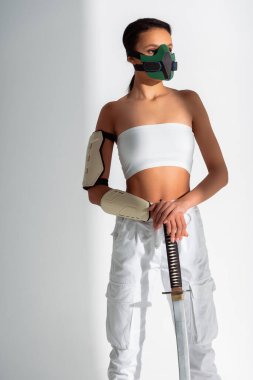 Beyaz arka planda kılıç taşıyan, güvenlik maskeli fütürist Afrikalı Amerikalı kadın.