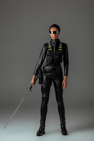 привлекательная футуристическая африканская американка в очках с мечом на сером
