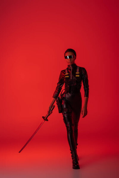 futuristic african american woman in glasses with sword on red background