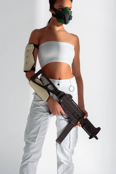 futuristic african american woman in safety mask with assault rifle on white background