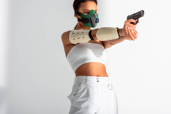 futuristic african american woman in safety mask aiming gun on white background