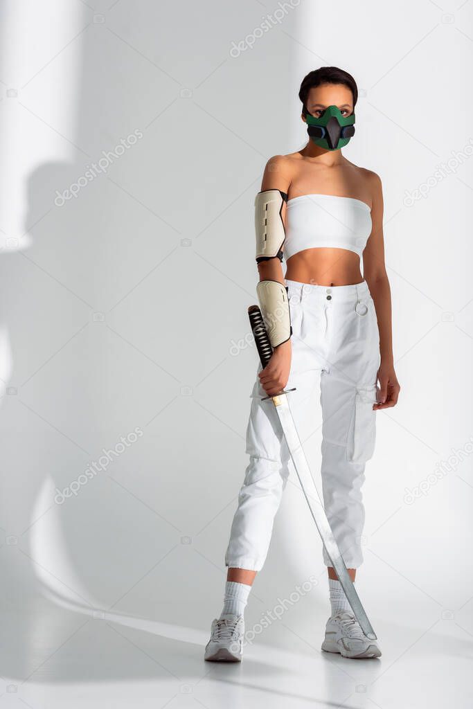 futuristic african american woman in safety mask with sword on white background