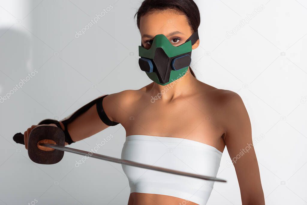 futuristic african american woman in safety mask with sword on white background