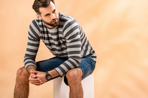 Bärtiger Junger Mann Gestreiftem Sweatshirt Sitzt Auf Weißem Würfel Auf — Stockfoto