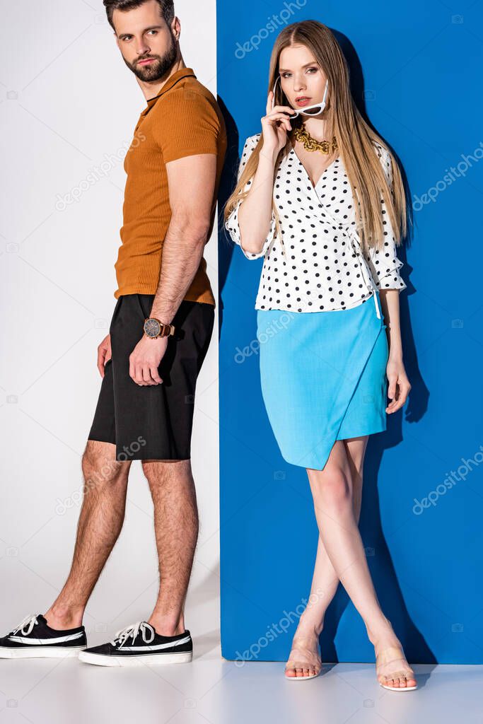 beautiful stylish couple posing in summer clothes and sunglasses on grey and blue
