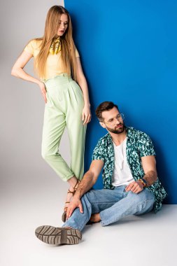Gri ve mavi renkte yaz kıyafetleri içinde poz veren şık bir çift. 