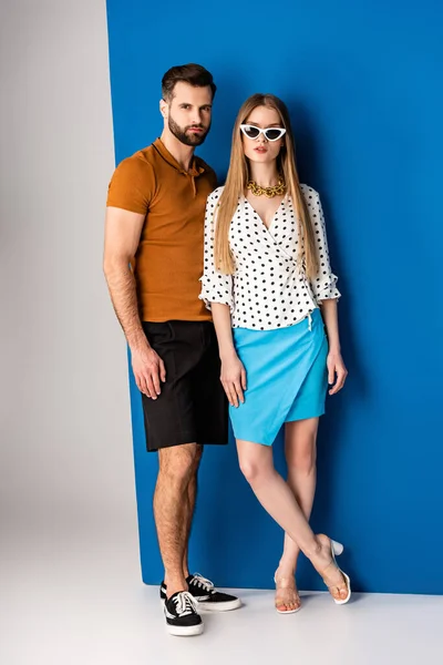 fashionable couple posing in summer clothes and sunglasses on grey and blue