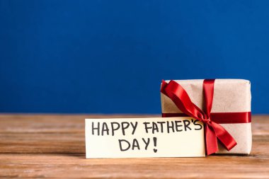 Mutlu Babalar Günü yazılı tebrik kartının seçici odağı ve mavi üzerinde kırmızı fiyonk bulunan hediye kutusu.