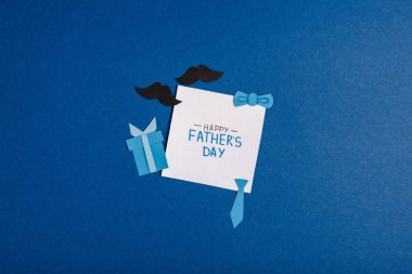 Mutlu Babalar Günü yazılı tebrik kartı ve mavi arka planda kağıt işçiliği dekorasyon unsurları.