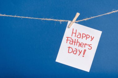 White paper greeting card with red lettering happy fathers day hanging on rope with clothespins isolated on blue clipart