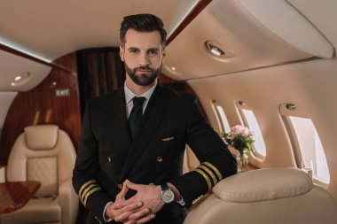 Yakışıklı, kendine güvenen üniformalı pilot özel jette dikilirken kameraya bakıyor.