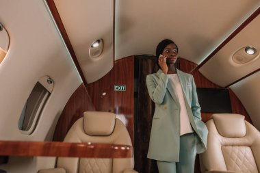 Genç, kendinden emin Afro-Amerikan iş kadını özel jette dururken akıllı telefondan konuşuyor.