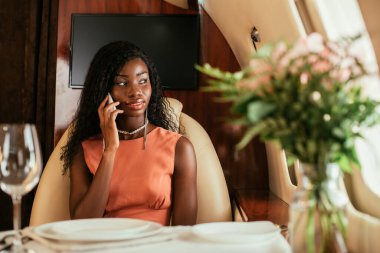Özel uçakta akıllı telefondan konuşan çekici Afrikalı Amerikalı kadının seçici odak noktası