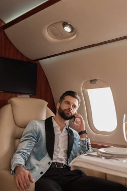 Kendine güvenen, zarif bir adam özel jetle seyahat ederken akıllı telefondan konuşuyor.