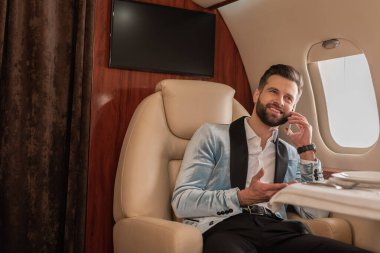 Gülümseyen, zarif bir adam özel jette seyahat ederken akıllı telefondan konuşuyor.