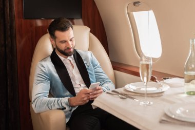 Özel bir jette servis masasında otururken akıllı telefondan konuşan zarif bir adam.