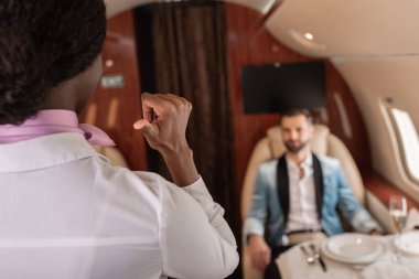 Afro-Amerikan hosteslerin arka görüntüsü başparmağıyla ve zarif bir adamın özel uçakta servis masasında oturduğunu gösteriyor.