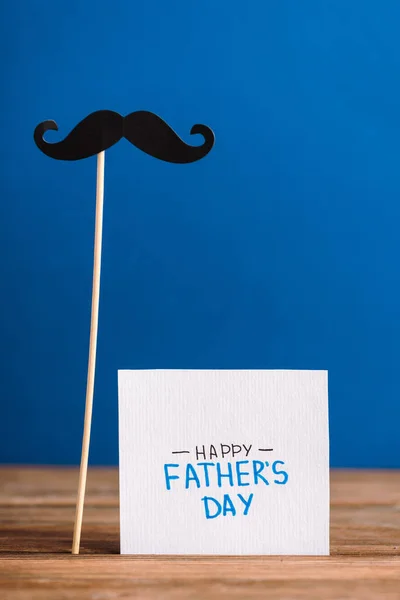 青で隔絶された幸せな父の日の文字を持つ段ボールとグリーティングカードから偽の口ひげの選択的な焦点 — ストック写真