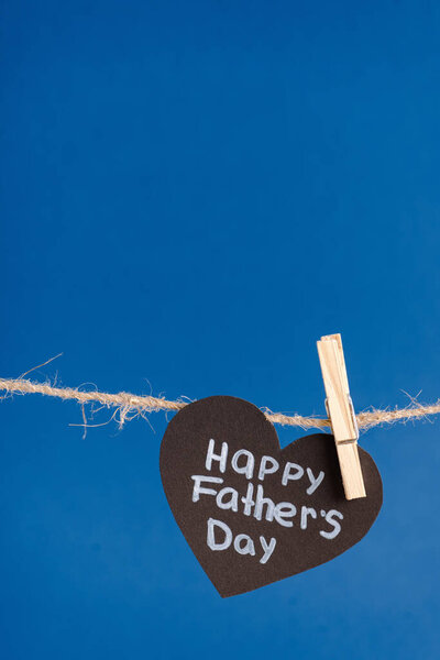 Black paper heart with white lettering happy fathers day hanging on rope with clothespins isolated on blue