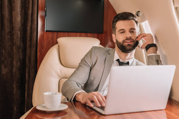 улыбающийся бизнесмен с помощью ноутбука во время путешествия на частном самолете
