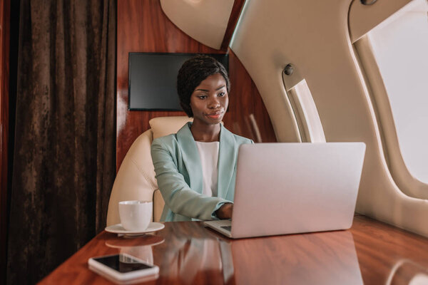 молодая, серьезная американская бизнесвумен, работающая на ноутбуке в частном самолете

