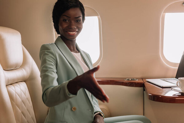 happy african american businesswoman showing greeting gesture with outstretched hand in private jet
