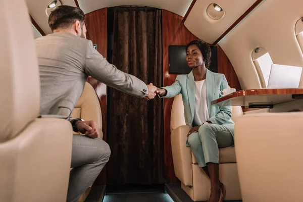 Foco Seletivo Dois Empresários Multiculturais Apertando Mãos Enquanto Viajam Avião — Fotografia de Stock