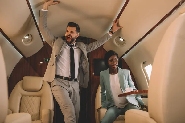 兴奋的商人一边尖叫一边摸天花板 同时害怕坐在私人飞机上的非洲裔美国女商人 — 图库照片