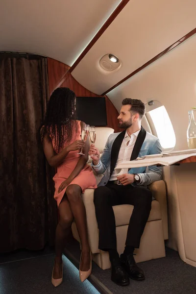 乘坐私人专机旅行时 雅致的跨种族夫妇一边喝着香槟酒一边碰杯 — 图库照片