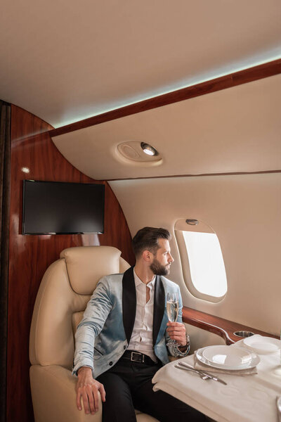 elegant, dreamy man holding glass of champagne and looking in porthole at served table