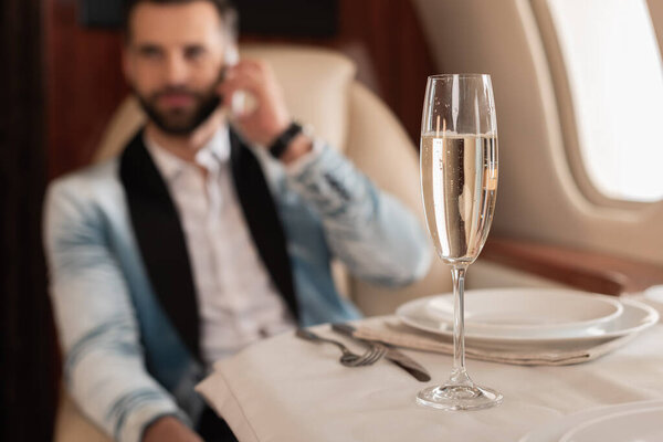 selective focus of elegant man talking on smartphone near glass of champagne in private jet