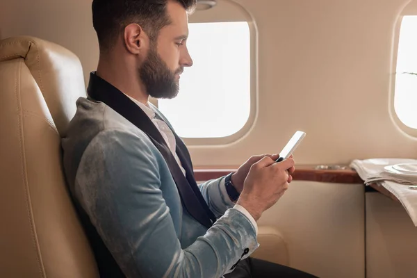 Zijaanzicht Van Elegante Jongeman Chatten Smartphone Prive Vliegtuig — Stockfoto