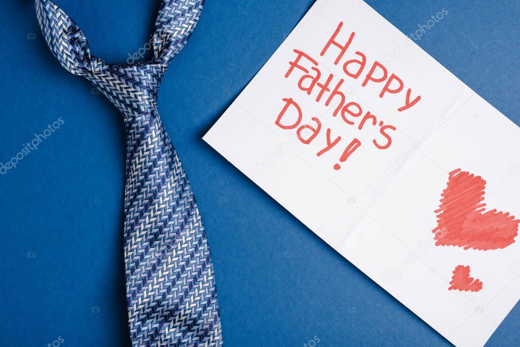 Top view of greeting card with lettering happy fathers day and red heart drown and mens tie on blue background