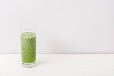 Beyaz ahşap yüzeyde camlı yeşil smoothie.