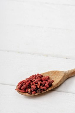 Tahta kaşıkta beyaz masada kuru goji üzümleri.