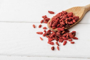 Tahta kaşıkta beyaz masada kuru goji üzümleri.