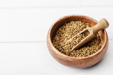 Beyaz yüzeyinde spatula bulunan ahşap bir kasede doğal bir çemen ağacı.