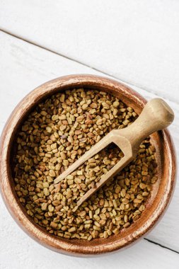Beyaz yüzeyinde spatula bulunan ahşap kâse içindeki doğal çemen ağacının en üst görüntüsü.