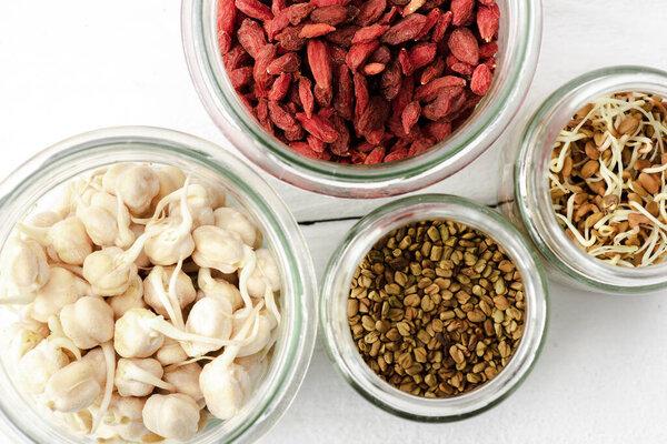 top view of goji berries and sprouts in glass jars on white wooden surface