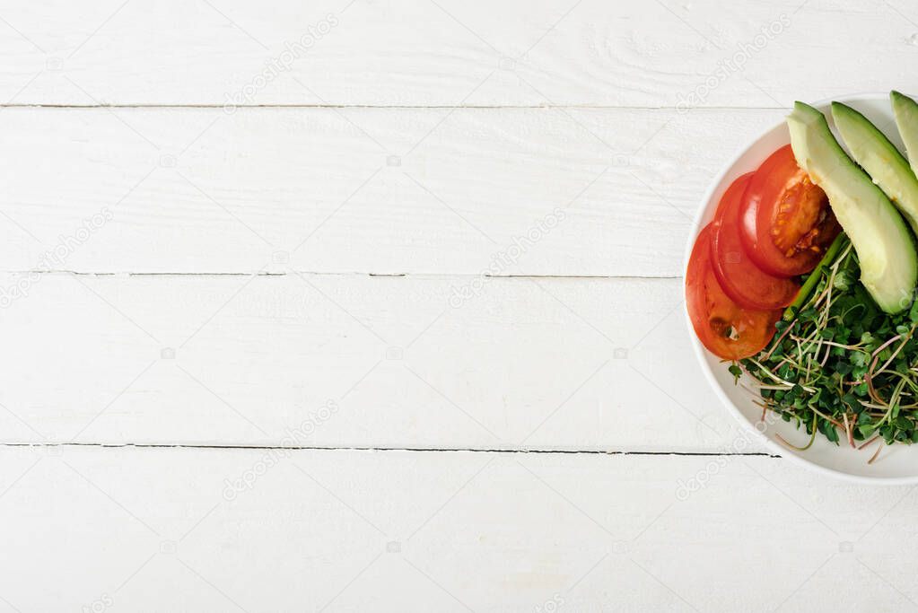 top view of tomato, avocado and microgreen in bowl on white wooden surface