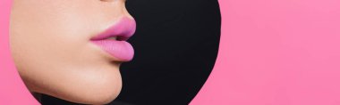 Cropped view of female face with pink lips in round hole in paper on black background, panoramic shot clipart